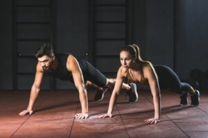 Sportswoman and sportsman doing push ups in gym in sports hall