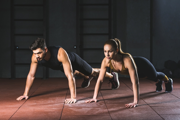 Sportswoman and sportsman doing push ups in gym in sports hall