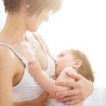 Young woman breastfeeding her baby on blurred background, closeup. Mom nursing and feeding baby. Close-up portrait of infant
