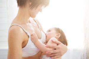 Young woman breastfeeding her baby on blurred background, closeup. Mom nursing and feeding baby. Close-up portrait of infant