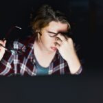 Young woman using computer at night rubs her eyes