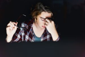 Young woman using computer at night rubs her eyes