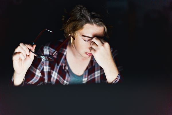Young woman using computer at night rubs her eyes