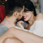 Beautiful couple smiling and sitting embraced face to face in chair spending their honeymoon time.