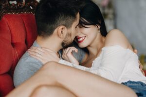 Beautiful couple smiling and sitting embraced face to face in chair spending their honeymoon time.