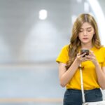 Young beautiful Asian woman using smartphone with internet and mobile app in subway station. Attractive teenage girl holding mobile phone and texting online message. Technology and city life concept.