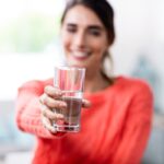 Young woman showing drinking glass with water
