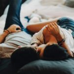 Attractive romantic couple laying on bed ,hugging and kissing in a cozy room.